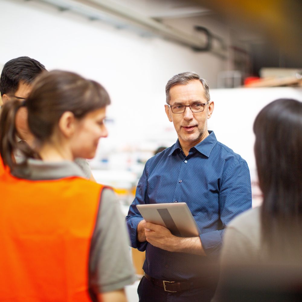 Consultant holding a tablet computer, talking with factory workers.