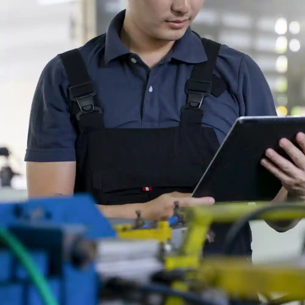 Person wearing black overalls, a blue shirt, holding a tablet.