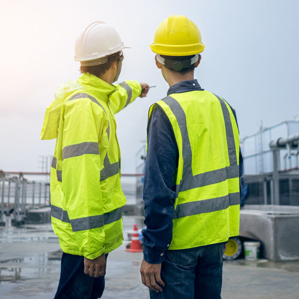 Two men in yellow vests looking at plant equipment.