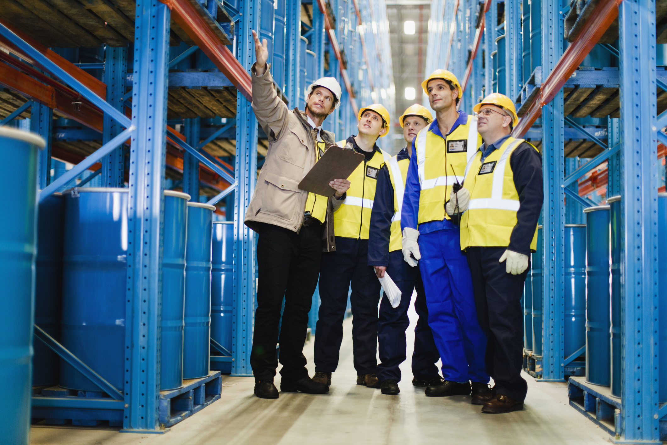 A group of factory workers gathered looking up in a warehouse.