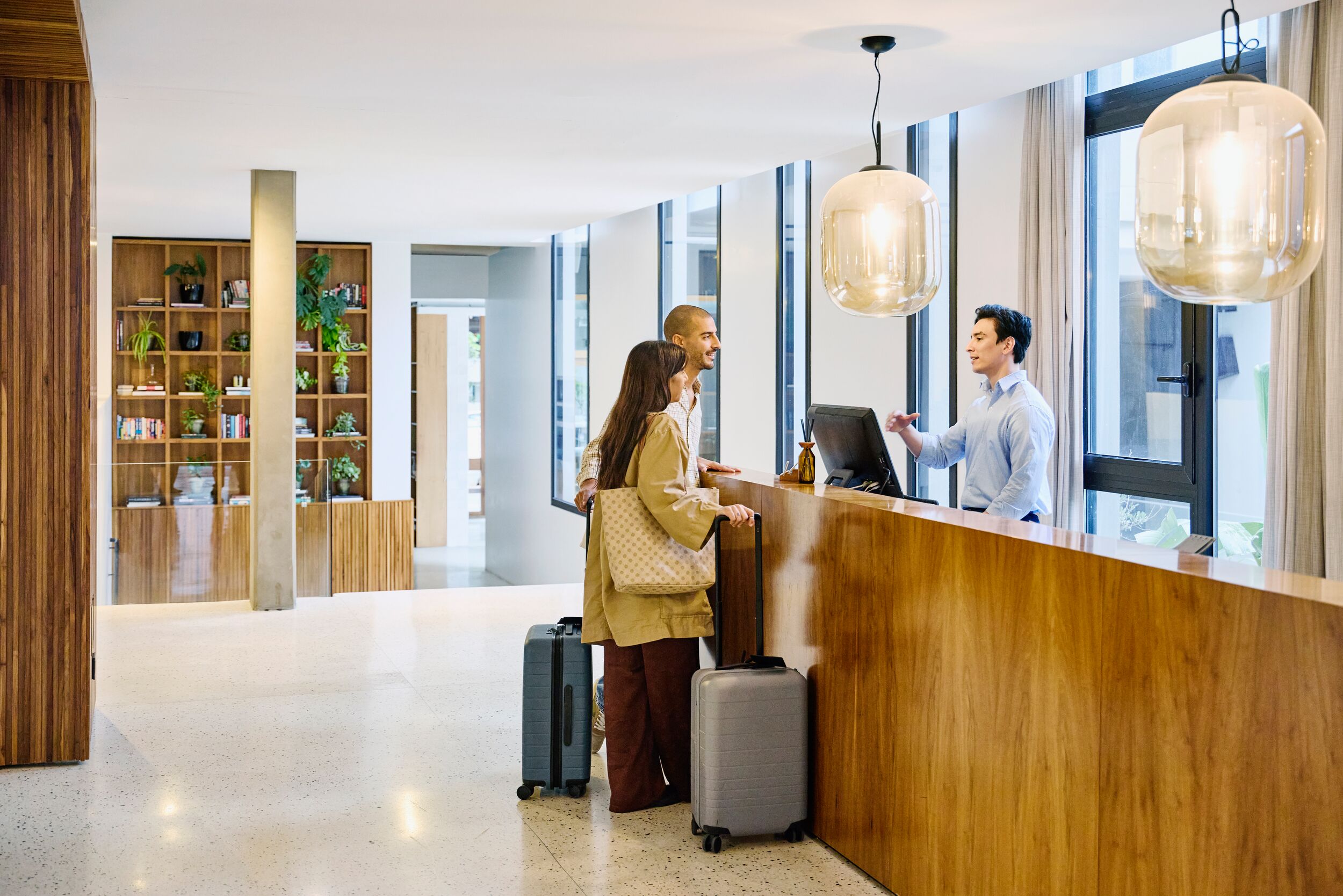 Male hotel receptionist checking in guests with suitcases at hotel lobby front desk.
