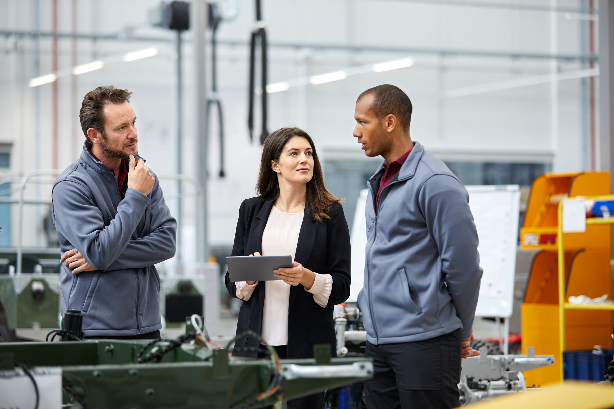 Three coworkers talking in a factory looking over a tablet.