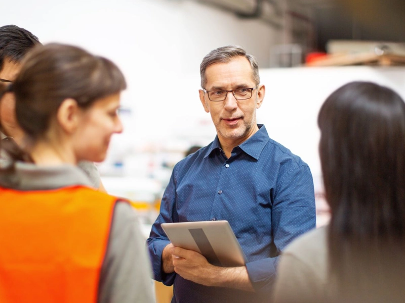 Consultant holding a tablet computer, talking with factory workers
