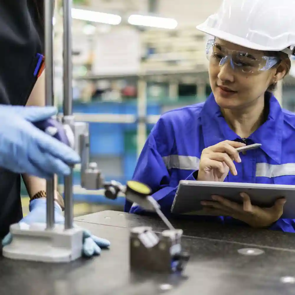 Technician overlooking work being done while holding a tablet and stylus pen and wearing a white hardhat.